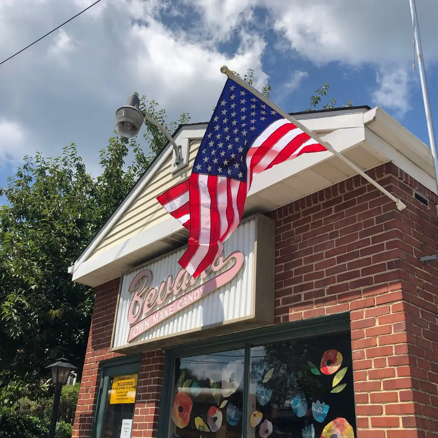 An American flag mounted on a brick storefront building, hanging over a candy shop sign, under a partly cloudy sky.