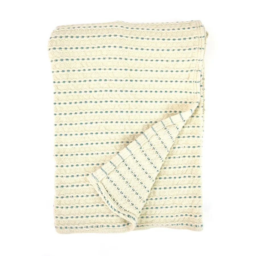 A folded cream cotton blanket with thin teal dotted stripes, corner turned back, shown against a white background.