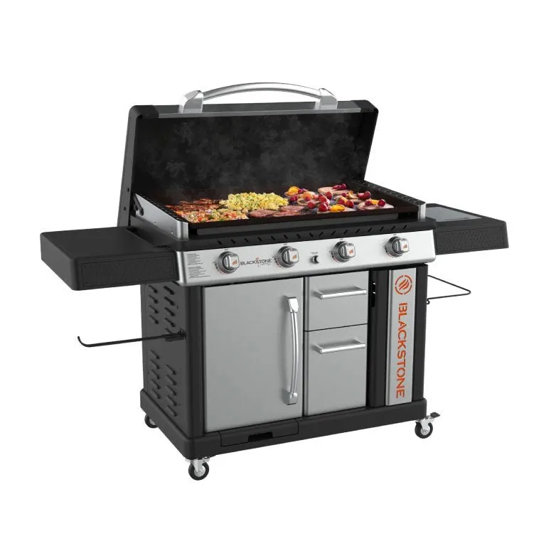 A stainless-and-black Blackstone 36-inch griddle with hood raised, cooking pancakes, bacon, eggs, and mixed vegetables on the flat-top surface, shot at an angle against a white background.