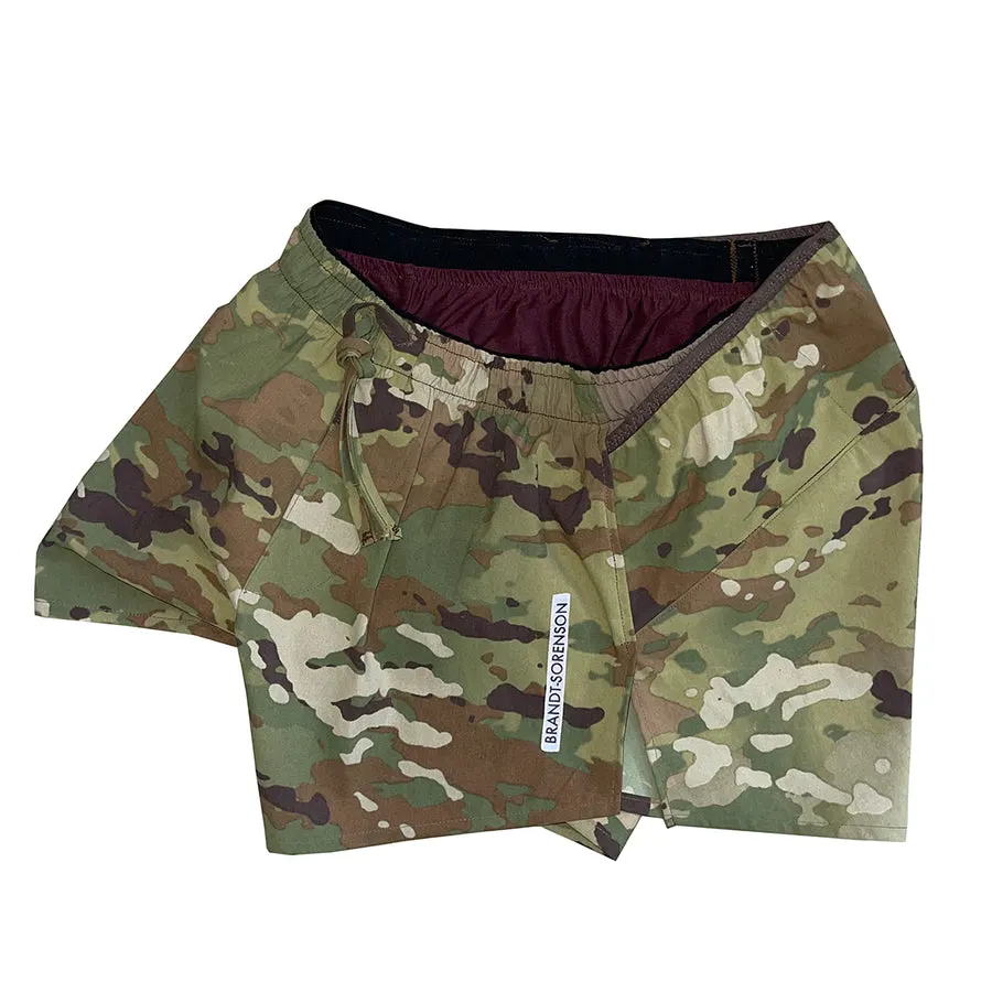 A pair of MultiCam camouflage split-hem running shorts with a maroon interior lining, laid folded against a white background, with a small woven Brandt-Sorenson tag visible on the leg.