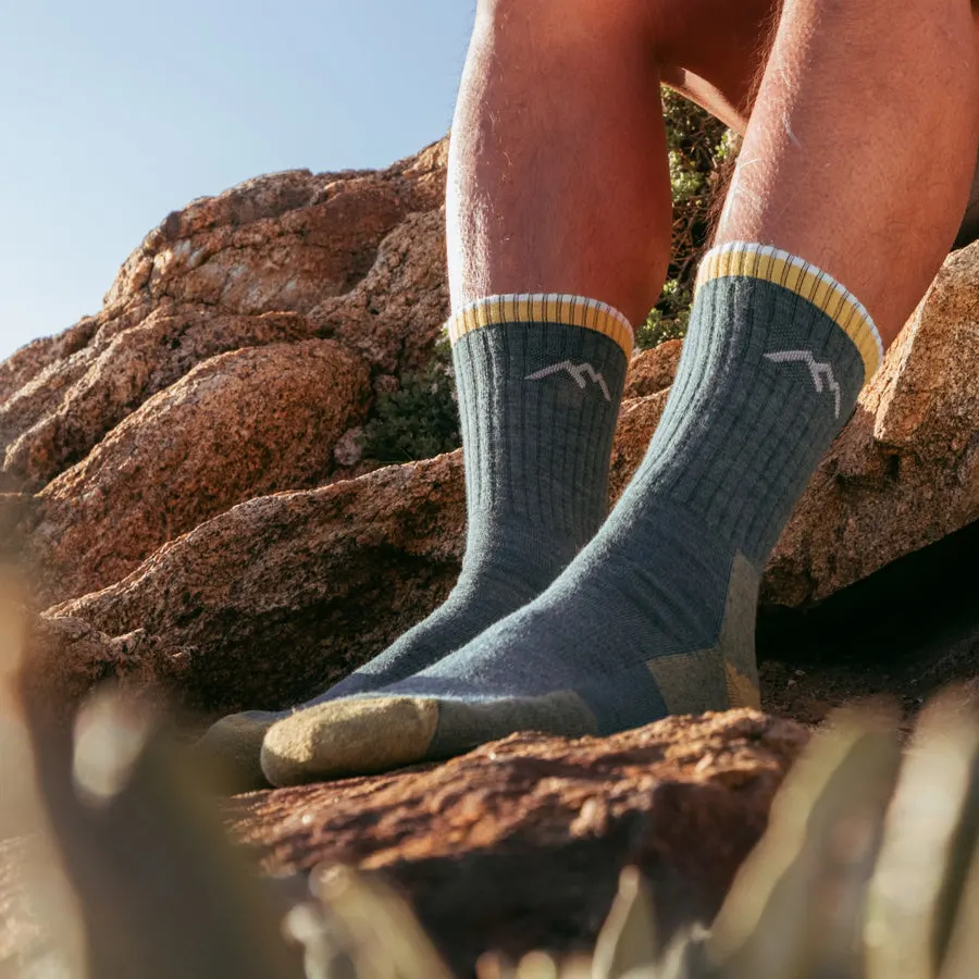Close-up of a pair of ribbed merino wool hiking socks in teal and gold, worn on bare legs while standing on a sunlit rock outdoors.
