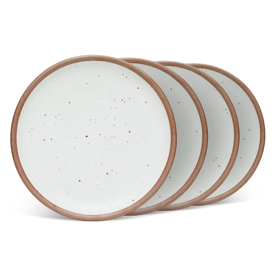 Four white speckled stoneware dinner plates with tan unglazed rims, fanned out and slightly overlapping on white.