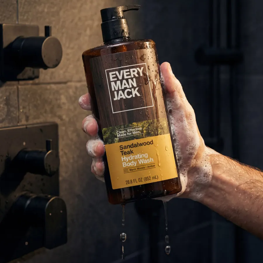 A soapy hand holds an amber Every Man Jack Sandalwood Teak Hydrating Body Wash bottle under running water in a dark-tiled shower.