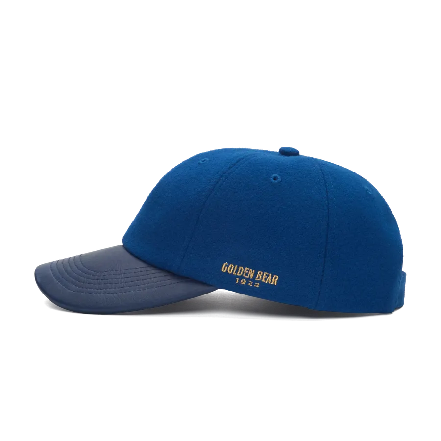 A blue melton wool baseball cap with a navy leather brim, shown in profile on white, with 'GOLDEN BEAR 1922' embroidered in gold on the side panel.