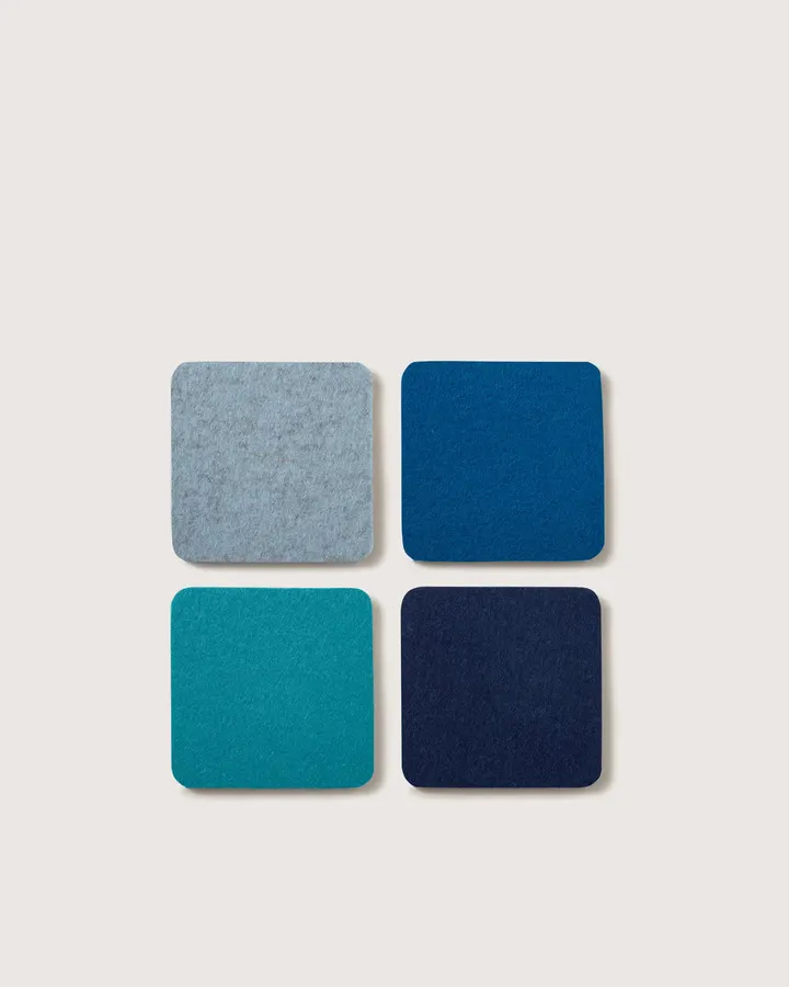 Four square felt coasters in light grey, teal, navy and blue, arranged in a 2x2 grid on a white background.