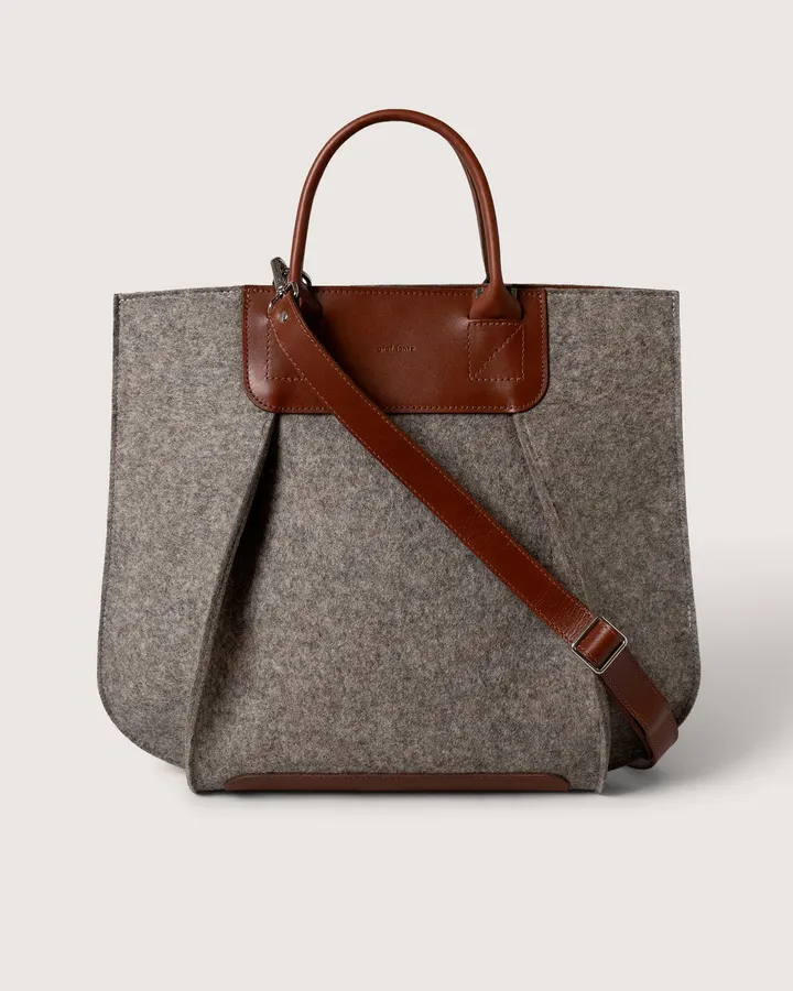 A heather-grey felt tote bag with a cognac leather handle, strap and trim, shown front-on against a white background.