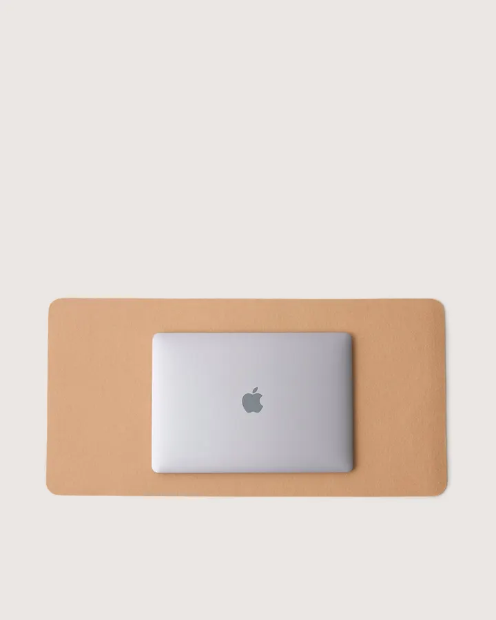 A tan felt desk pad with a silver laptop resting on top of it, seen from above against a white background.