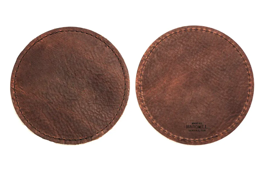 Two round brown leather coasters with stitched edges, one showing the front and one the back stamped 'Made by Hardmill, Seattle USA', against a white background.