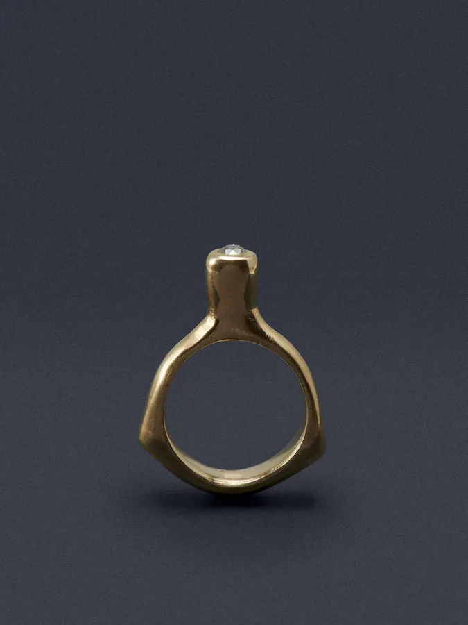 A hammered-texture 14k gold ring with an angular wing-like shank set with a single small round diamond, shot against a dark charcoal background.