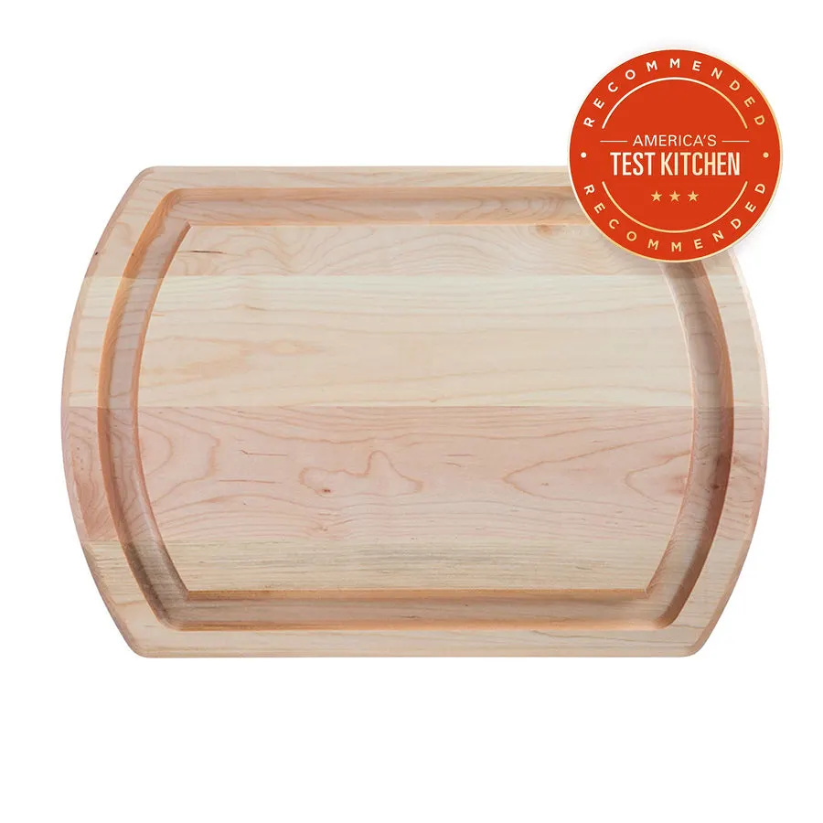 A large oval-cornered maple wood carving board with a juice groove, viewed from above, with a red America's Test Kitchen "Recommended" seal in the corner.