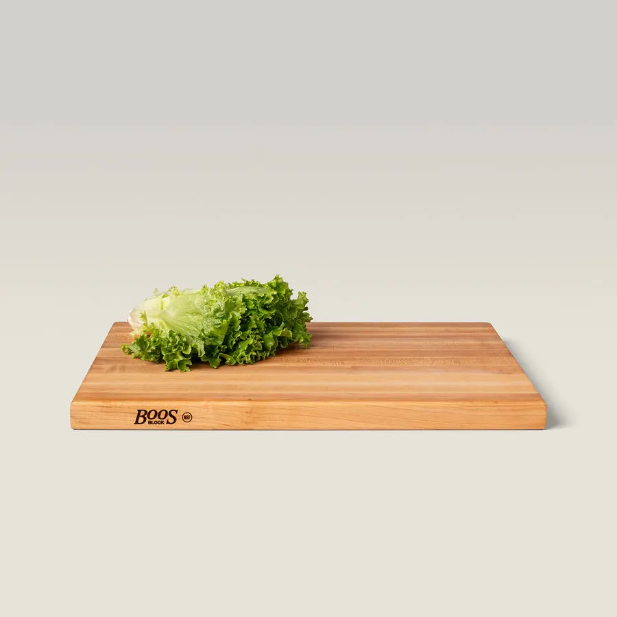 A rectangular maple end-grain cutting board branded "BOOS BLOCK" on its edge, shown at an angle on a plain background with a head of green leaf lettuce resting on top.