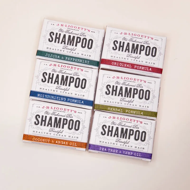 Six boxed bars of J.R. Liggett's Old-Fashioned Bar Shampoo arranged in a flat-lay grid, each in a different scent variant with a different colored label stripe (jojoba and peppermint, original formula, moisturizing formula, herbal formula, coconut and argan oil, tea tree and hemp oil).