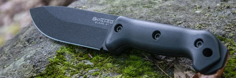 A black fixed-blade knife with a black rubberized handle resting on a moss-covered rock, blade angled toward the camera.