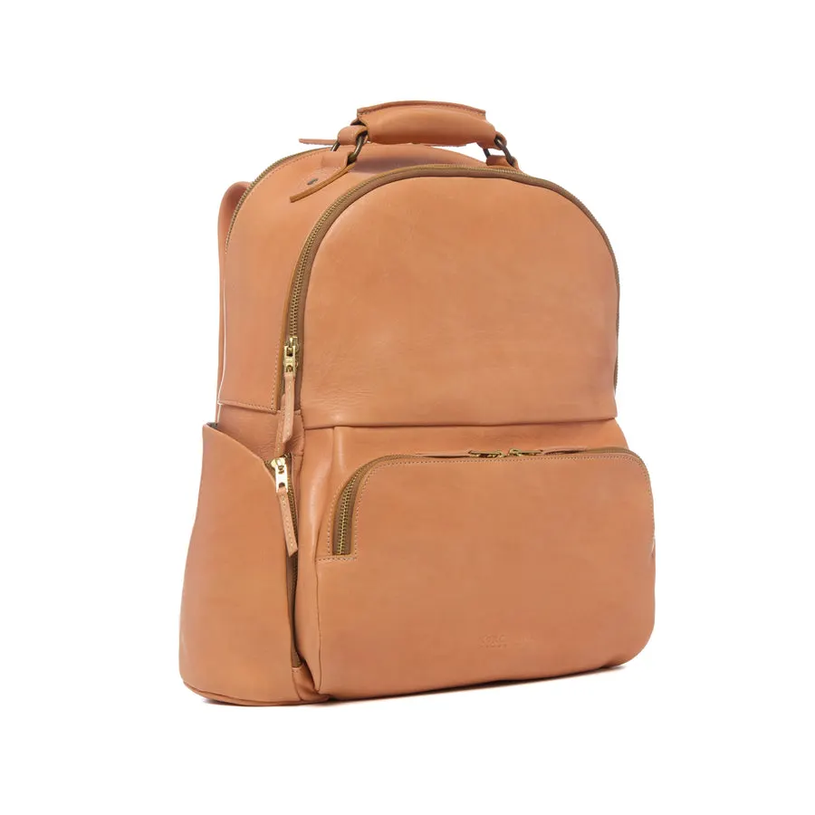 A tan leather backpack with a rounded top, brass zippers, a top carry handle, and a front zip pocket, shown at a three-quarter angle against a white background.