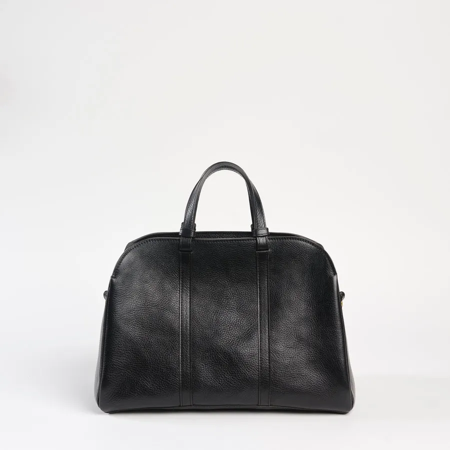 A black pebbled-leather duffel bag with rolled top handles and vertical seam stitching, photographed standing upright against a plain light gray background.