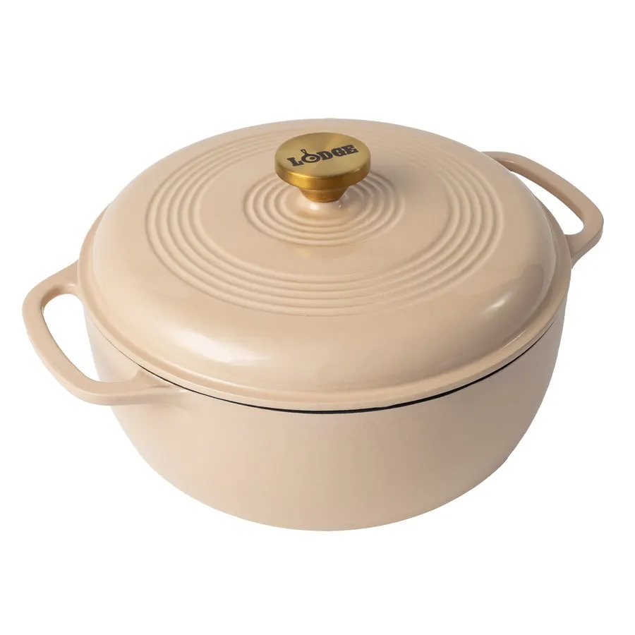 A tan (latte) enameled cast iron Dutch oven with lid and a brass Lodge-branded knob, shown at an angle on a white background.