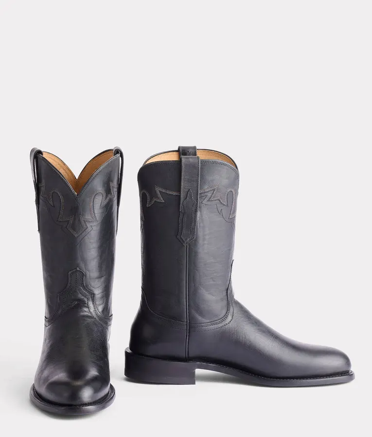 A pair of black leather roper-style boots with a low stacked heel and rounded toe, shot on a white background.
