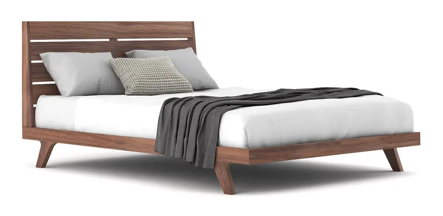 A walnut wood bed frame with a slatted headboard, shown in profile on a white background with white sheets, grey pillows, and a folded grey throw.