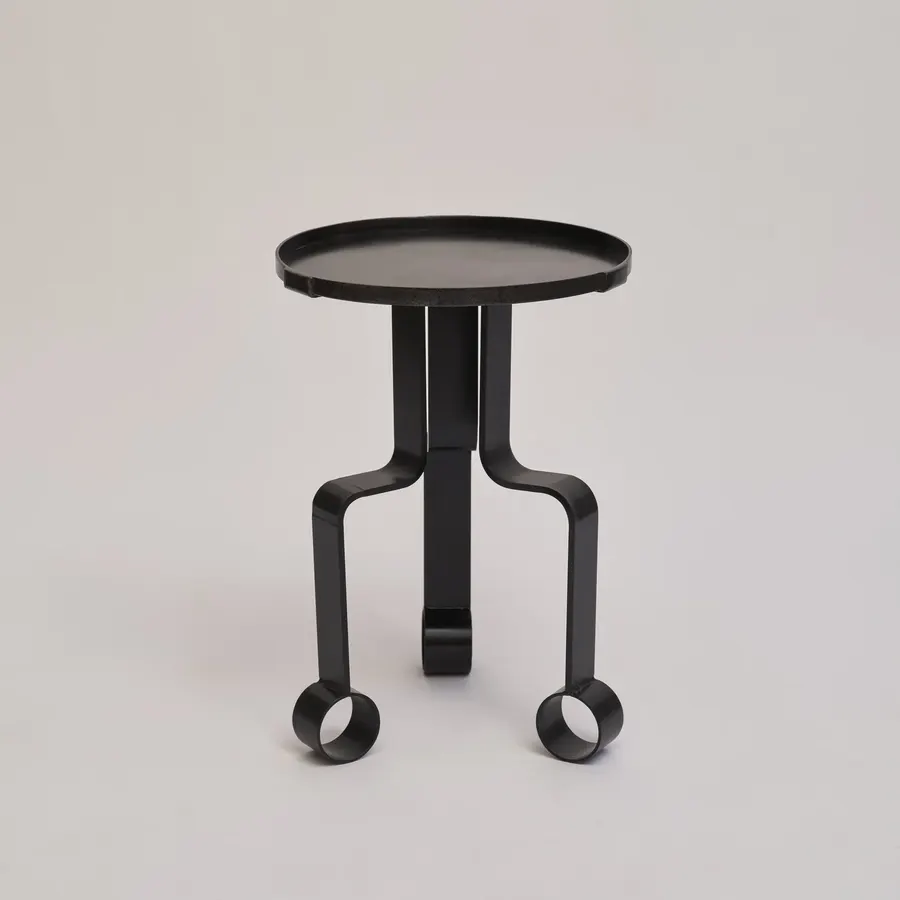 A small round black metal side table with a tripod base of curved legs ending in ring-shaped feet, shown against a plain light grey background.