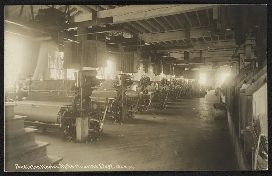 Black-and-white postcard photograph of a wool mill's weaving department, rows of mechanical looms under a wood-beamed ceiling, captioned "Pendleton Woolen Mills Weaving Dept."