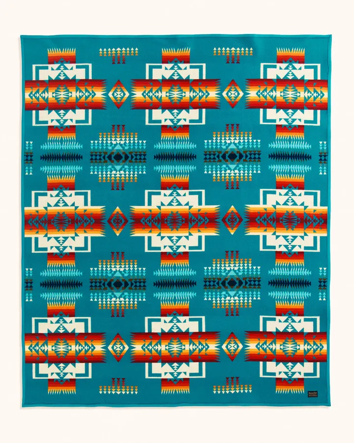 A folded wool blanket in the Chief Joseph pattern, turquoise ground with red, orange, and cream geometric bands, photographed flat against a pale background.
