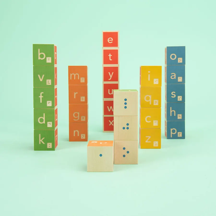 Stacks of colorful wooden alphabet blocks with raised Braille dots beside printed letters, on a mint-green background.