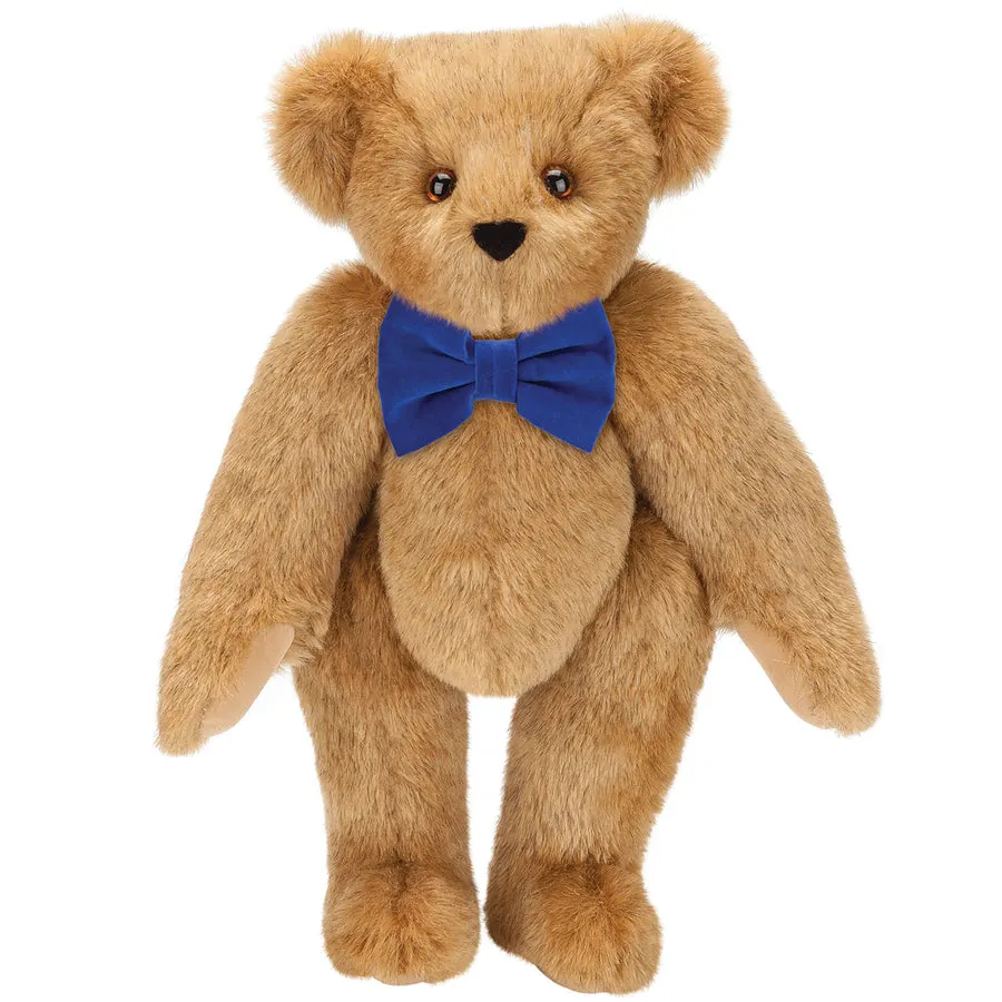 A tan jointed teddy bear with a royal blue velvet bow tie, standing upright against a plain white background.