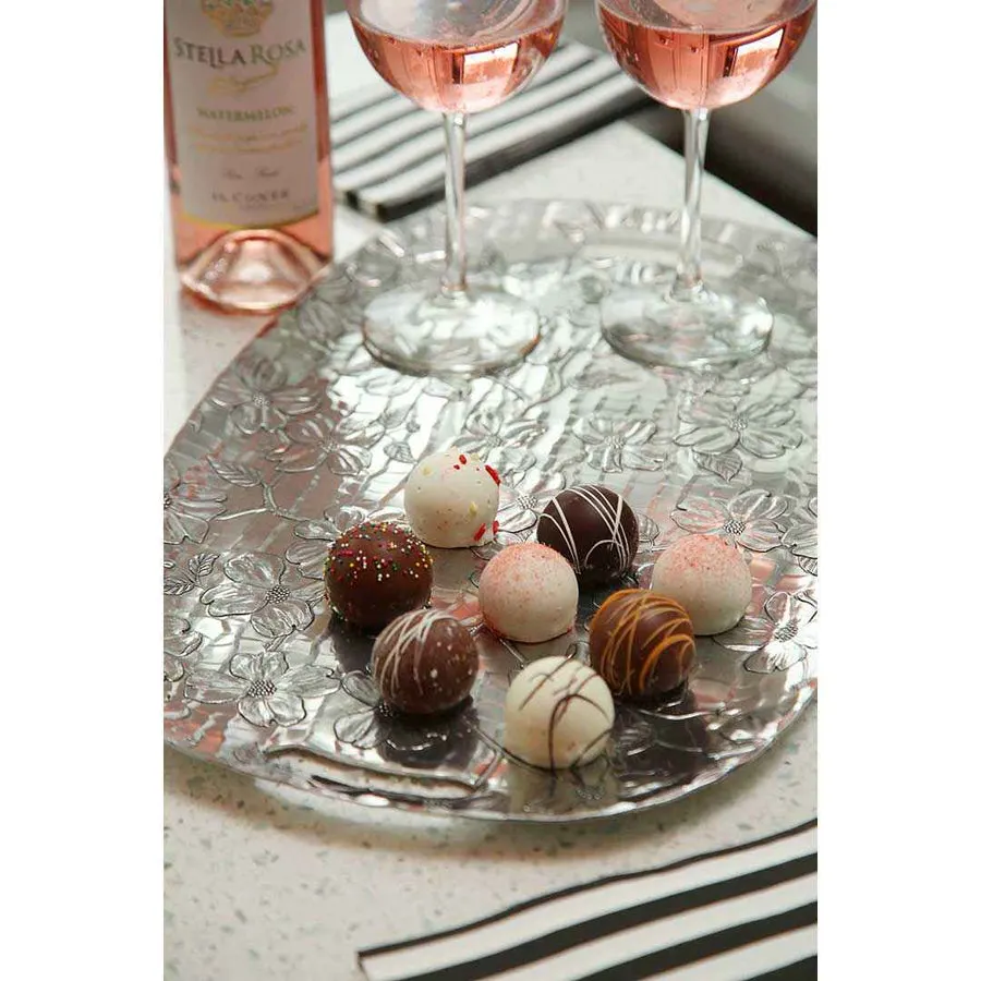 A hand-hammered aluminum serving tray with an embossed dogwood-flower pattern, styled on a countertop with chocolate truffles and two glasses of rose wine.