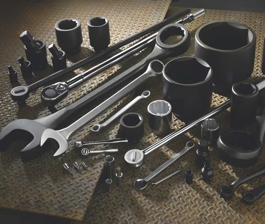An overhead, dramatically lit spread of chrome and black-oxide wrenches, sockets and a ratchet arranged on diamond-plate steel.